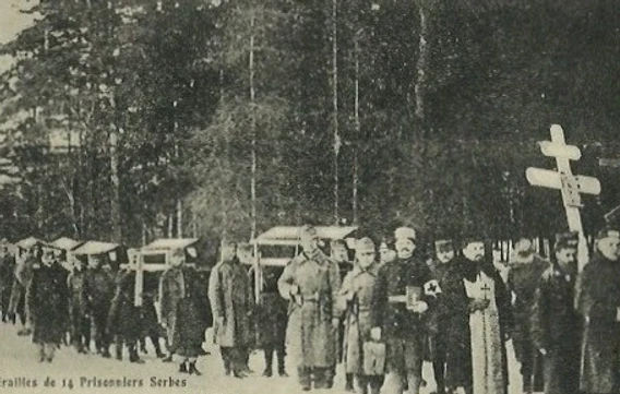 A black and white photograph from the WWI POW camp Aschach an der Donau in Austria. The photograph shows a funeral procession for at least 5 coffins, under armed guard.